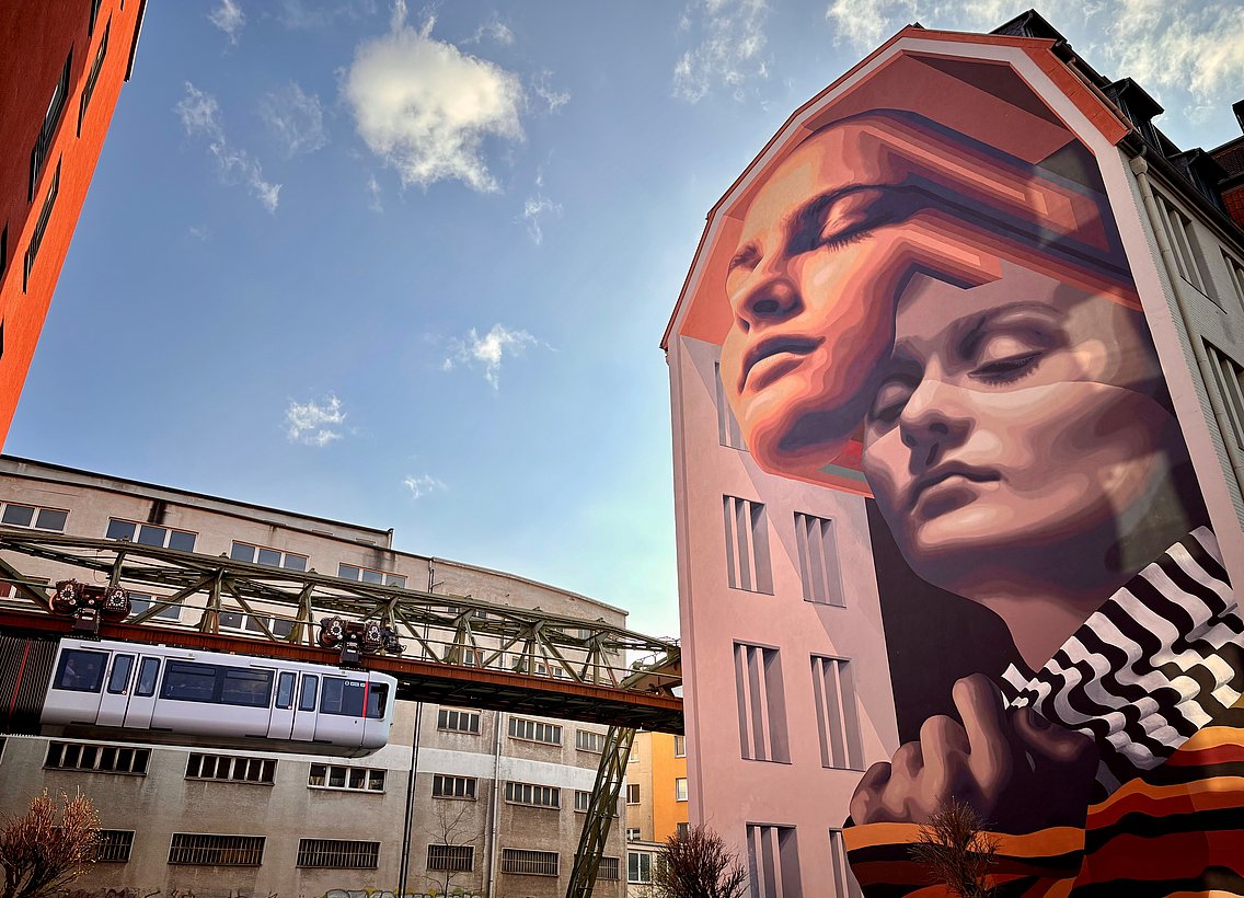 Mural in der Hofaue, das zwei Frauengesichter zeigt, mit Schwebebahn im Hintergrund- Wuppertal