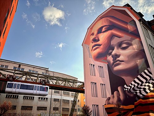 Mural in der Hofaue, das zwei Frauengesichter zeigt, mit Schwebebahn im Hintergrund- Wuppertal